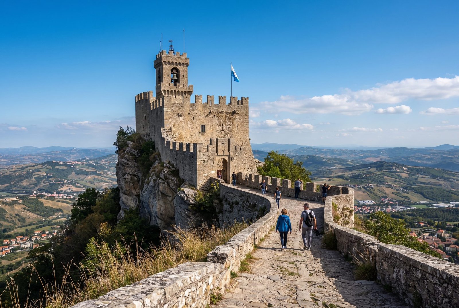 Guaita Tower on Mount Titano with tourists on the stone walkway and Apennine hills behind, San Marino